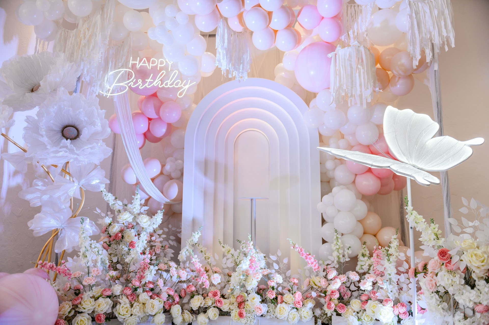 Birthday party for baby girl on a background photo wall. Arch decoration pink, white balloons, text Happy Birthday, flowers, paper decor butterfly. Children's photo zone.